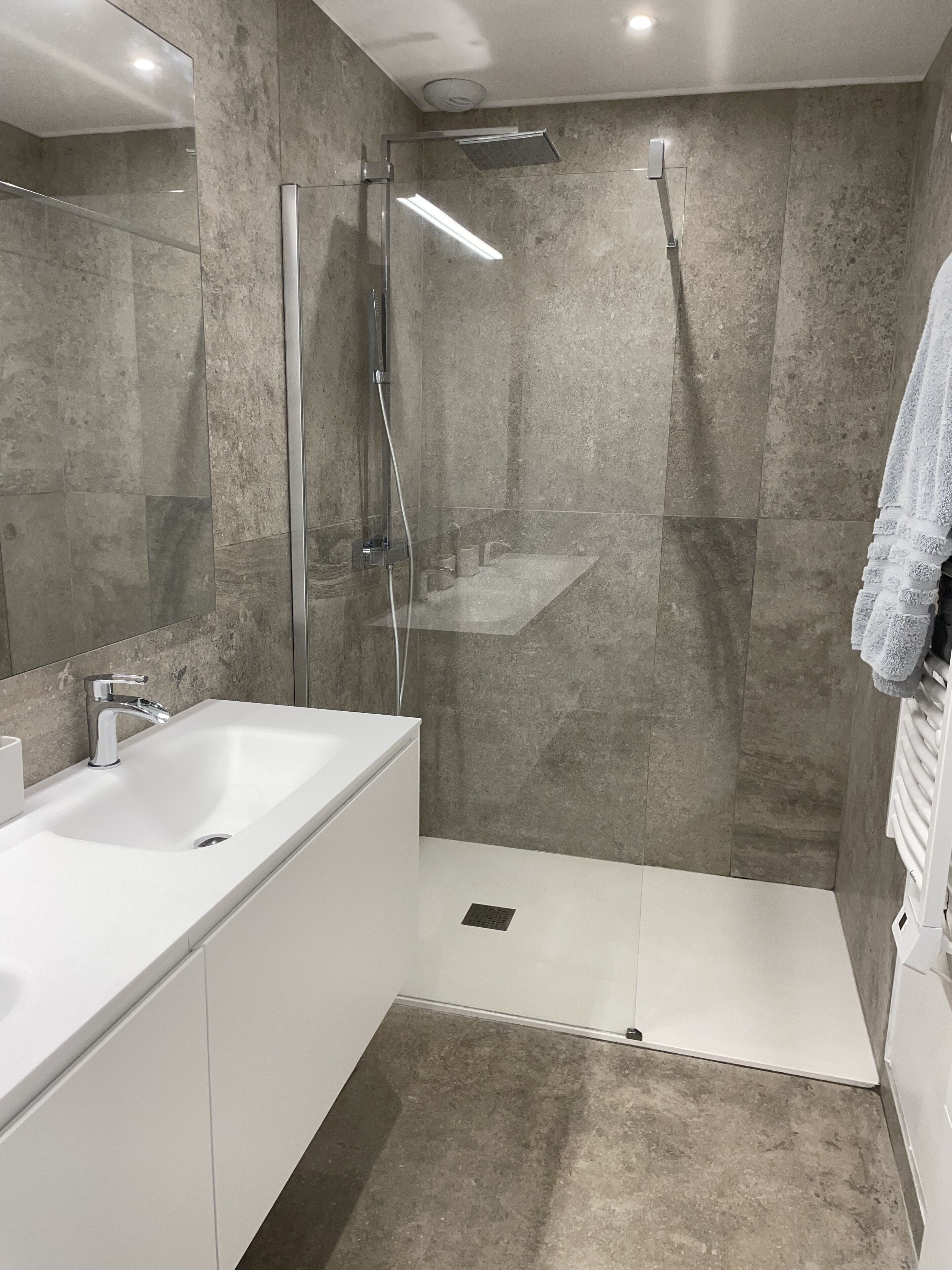 A modern bathroom with a glass-enclosed shower, a white sink, and a large mirror.