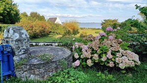 Ein Garten mit Hortensienbüschen, einer Steinmauer und einem Gewässer im Hintergrund.