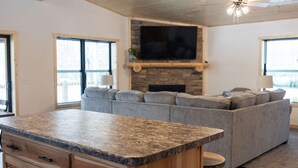 A modern living room with a stone fireplace, grey sectional sofa, and a wooden island with drawers. - NEW 5BR Cabin (Wetmore)