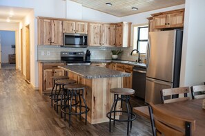 A modern kitchen with wooden cabinets, a stainless steel refrigerator, and a central island with stools. - NEW 5BR Cabin (Wetmore)