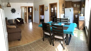 A spacious living area with a dining table, chairs, a sofa, and a kitchen area with wooden cabinets and a refrigerator. - Grace Land Cottages (West Nipissing)