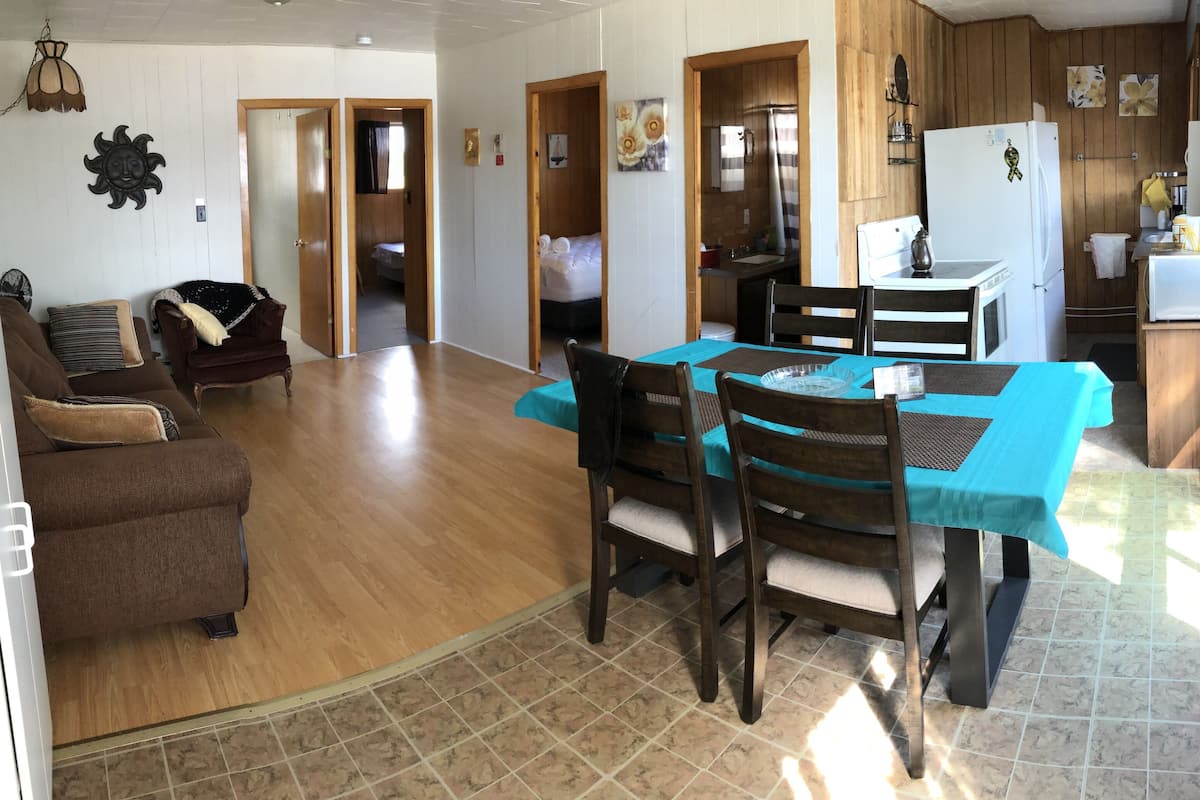 Ett rymligt vardagsrum med ett matbord, stolar, en soffa och ett köksområde med träskåp och ett kylskåp.