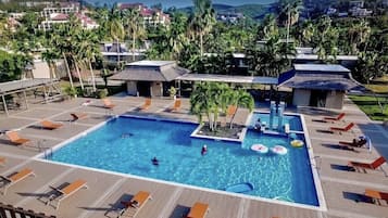 Ein Swimmingpool mit Liegestühlen und Sonnenschirmen, umgeben von Palmen und Gebäuden.
