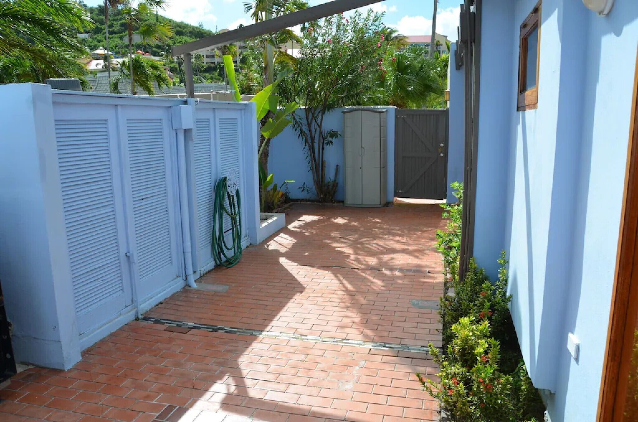 A courtyard with a brick floor, white shutters, and a blue wall.