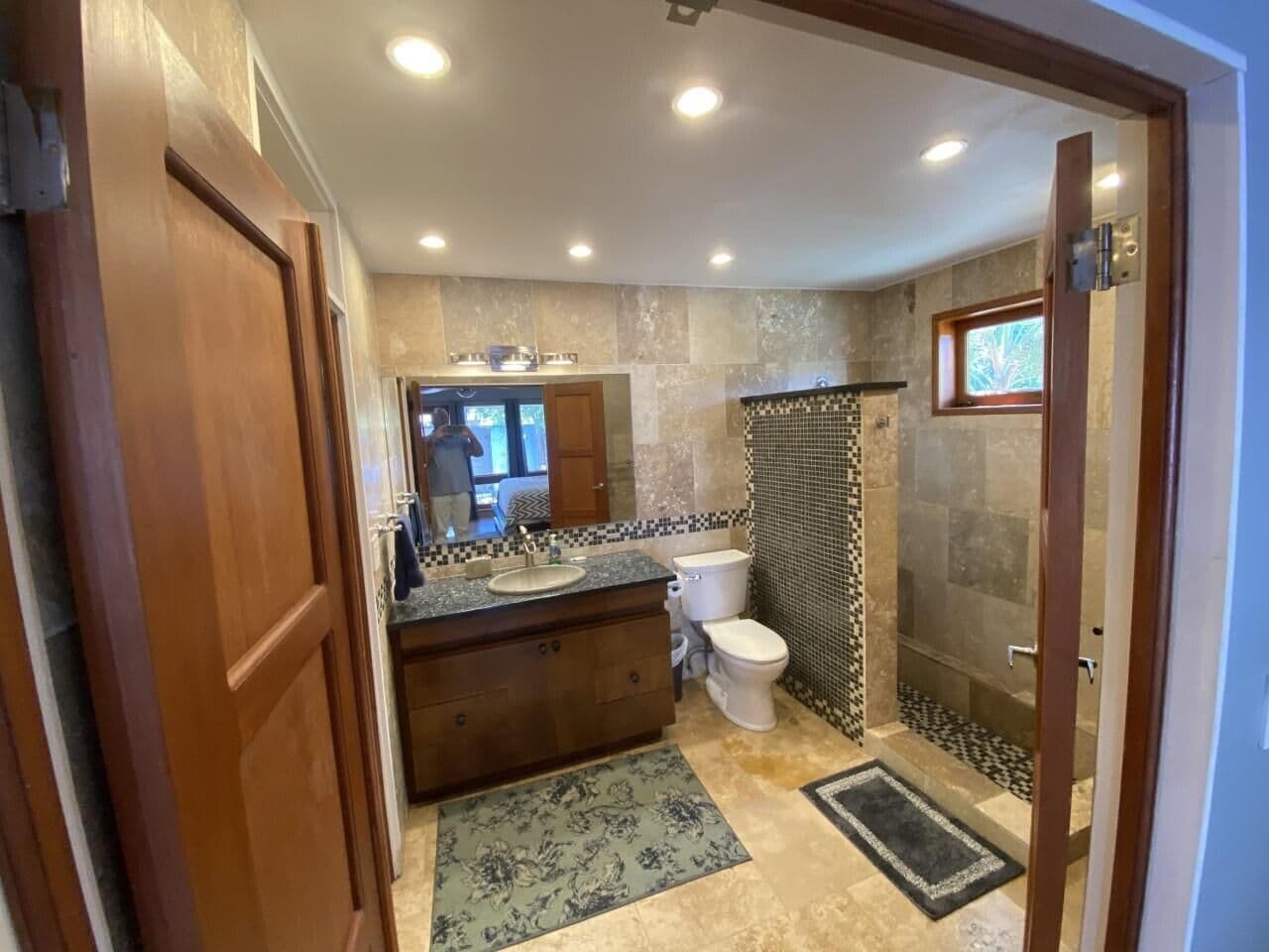 Ein Badezimmer mit einem Holzwaschtisch, einer Toilette, einer Dusche mit Glastür und einer gefliesten Spritzschutzwand.