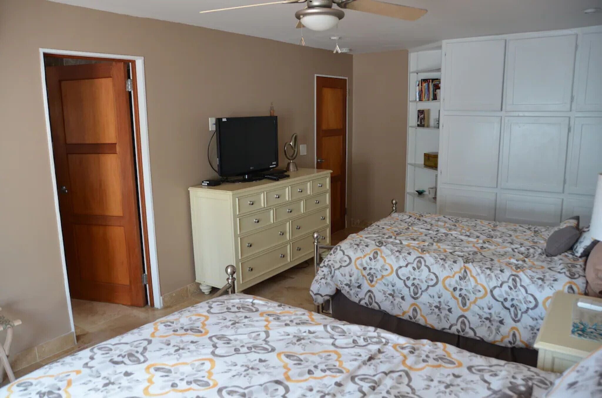 Un dormitorio con dos camas, un tocador, un televisor y un ventilador de techo.