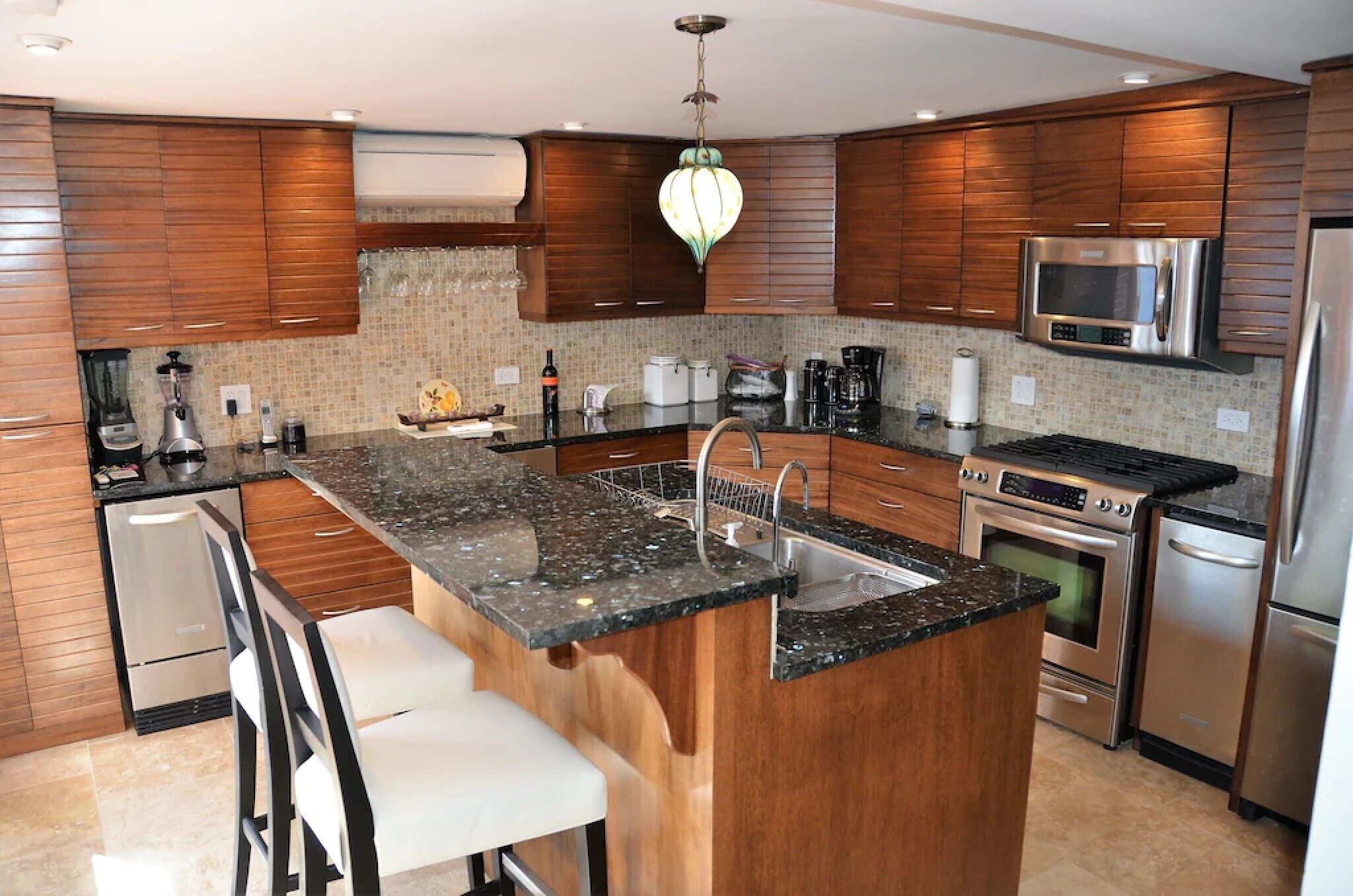 Una cocina moderna con armarios de madera, encimera de granito, electrodomésticos de acero inoxidable y una isla central con taburetes de bar.