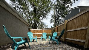 Un patio con baldosas de piedra, cuatro sillas Adirondack turquesa y una valla de madera.
