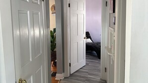 Un pasillo con puertas blancas, una lámpara en el techo y una planta en la esquina.
