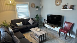 Una sala de estar moderna con un sofá negro, una mesa de centro de madera, un sillón rojo, un televisor y decoración en la pared.