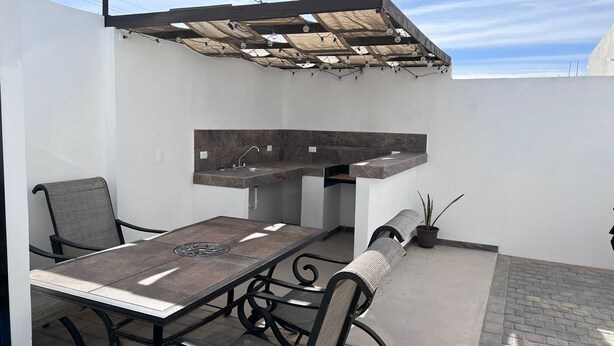 Een buitenkeuken met een eettafel en stoelen, een inbouwspoelbak en een pergola erboven.
