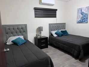 Une chambre avec deux lits, une table de chevet, une lampe et un tableau représentant un paon.