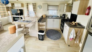Een compacte keuken met een spoelbak, fornuis en magnetron. Er is een eettafel met stoelen en een klein vloerkleed.