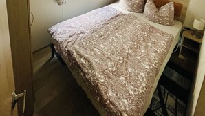 Een slaapkamer met een bed, een raam met gordijnen, een houten kledingkast en een nachtkastje.