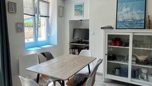A dining area with a wooden table and white chairs, a TV, and a cabinet with dishes. - Near Paimpol, Apartment 200m from Bréhec Beach (Plouézec)