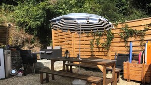 A wooden outdoor seating area with a table, benches, and a striped umbrella. - Near Paimpol, Apartment 200m from Bréhec Beach (Plouézec)