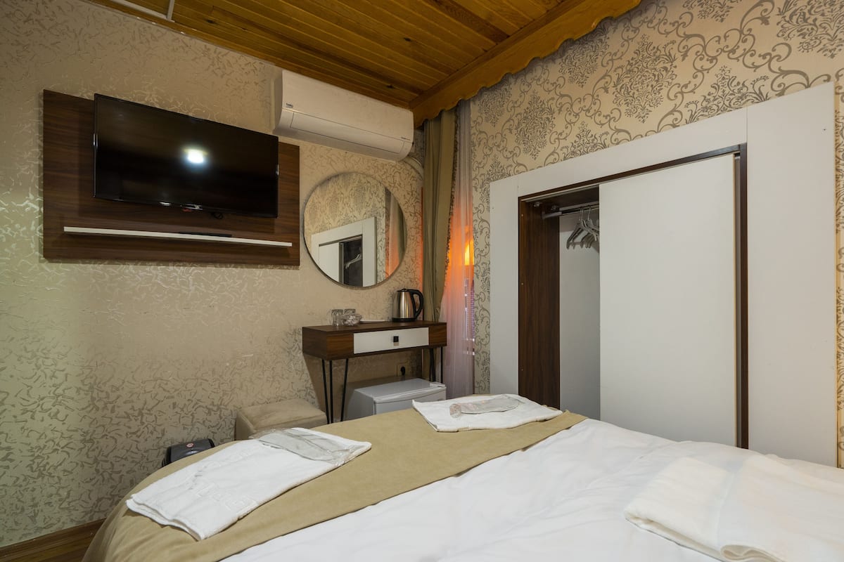 A hotel room with a bed, a TV mounted on the wall, a bedside table with a lamp, and a wardrobe.