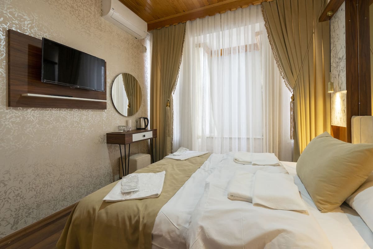 A hotel room with a bed, a TV mounted on the wall, a desk with a mirror, and a window with curtains.