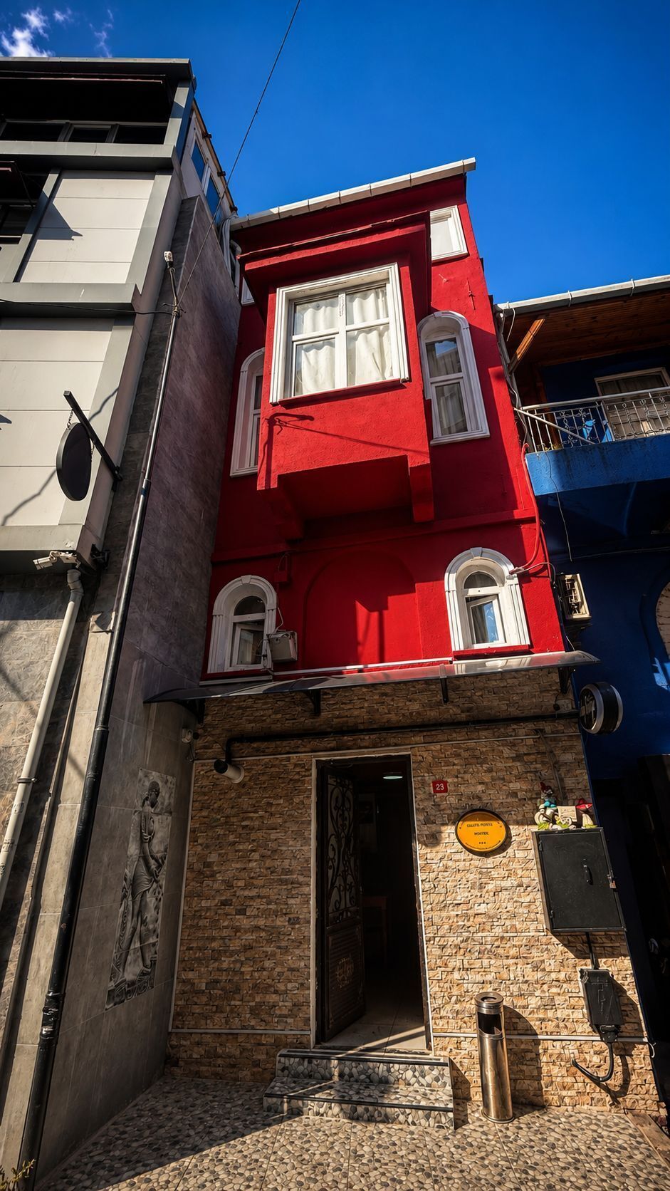 A red building with a stone facade, a door, and a small outdoor area with a metal trash can.