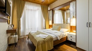 Habitació d'hotel amb sostre de fusta, llit amb roba blanca, tauleta de nit amb una làmpada, armari i un mirall gran.