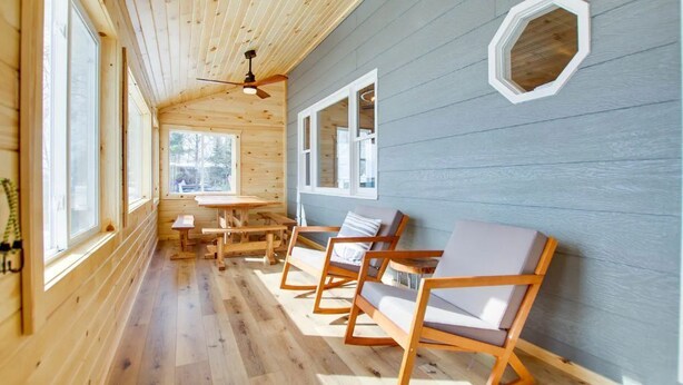 L’intérieur d’une cabane avec des murs en bois, un ventilateur de plafond, une table à manger et deux fauteuils.