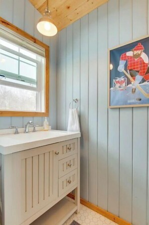 A bathroom with a white vanity, a window, and a painting of a man in a red shirt.