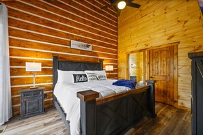 A wooden cabin-style bedroom with a bed, nightstands, and a wooden door.