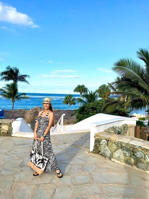 Mulher com vestido de padrão de zebra em área pavimentada com vista para o oceano e palmeiras.