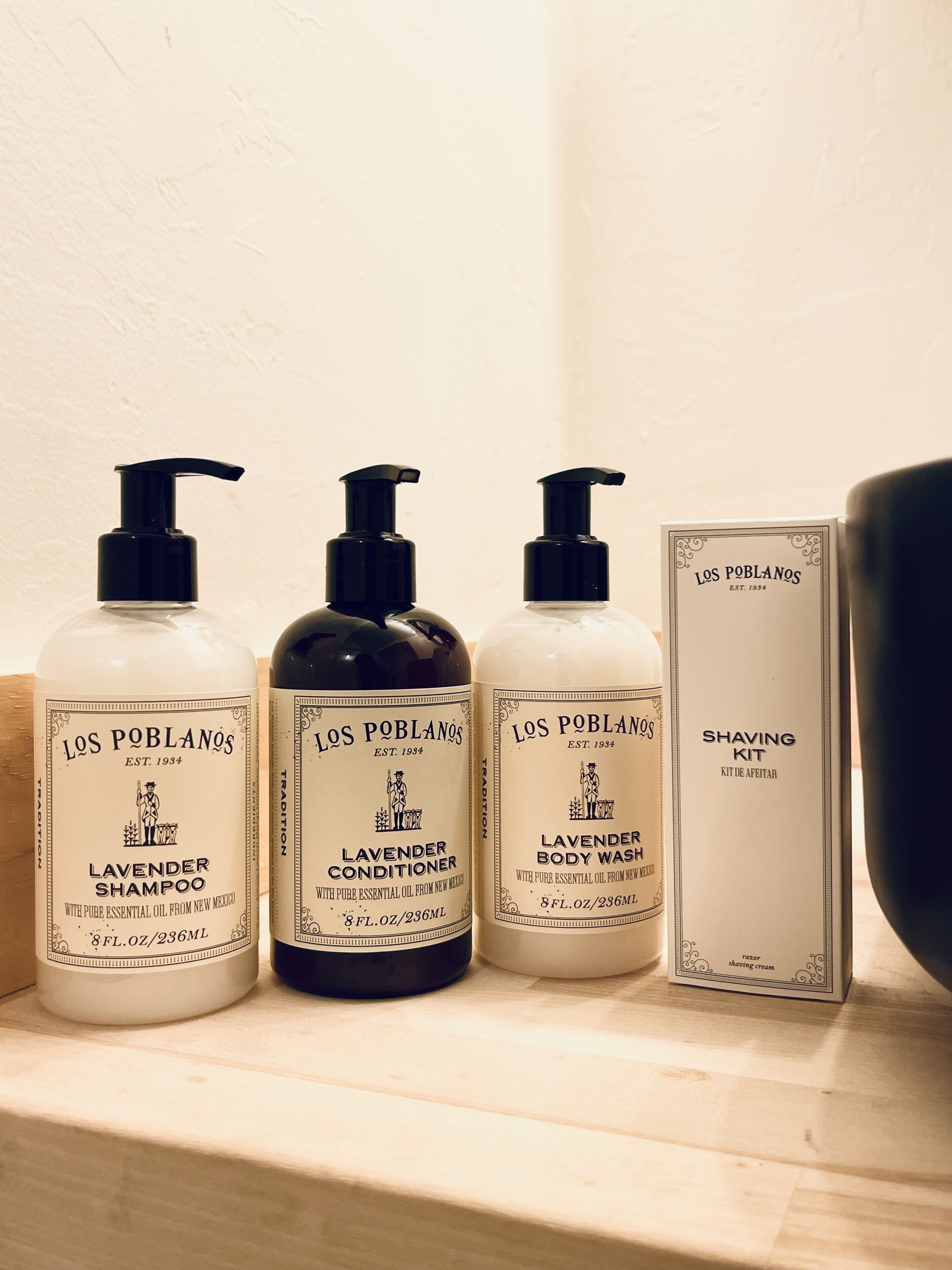 Tres botellas de productos Los Poblano y un kit de afeitado sobre una estantería.