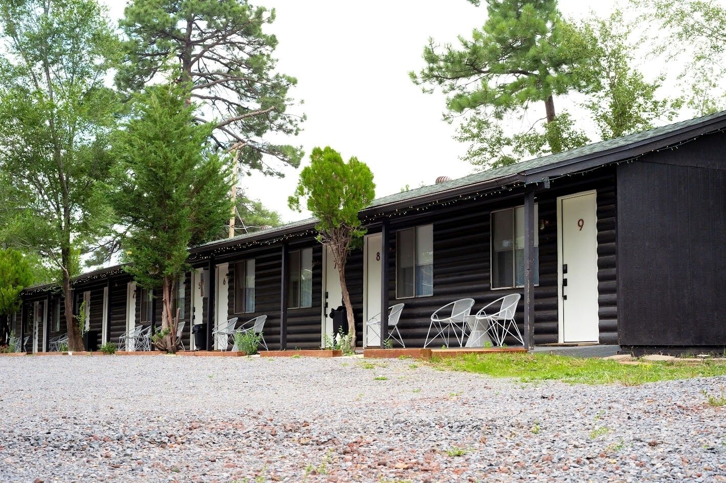 A row of log cabin-style cabins with outdoor seating and a gravel driveway.