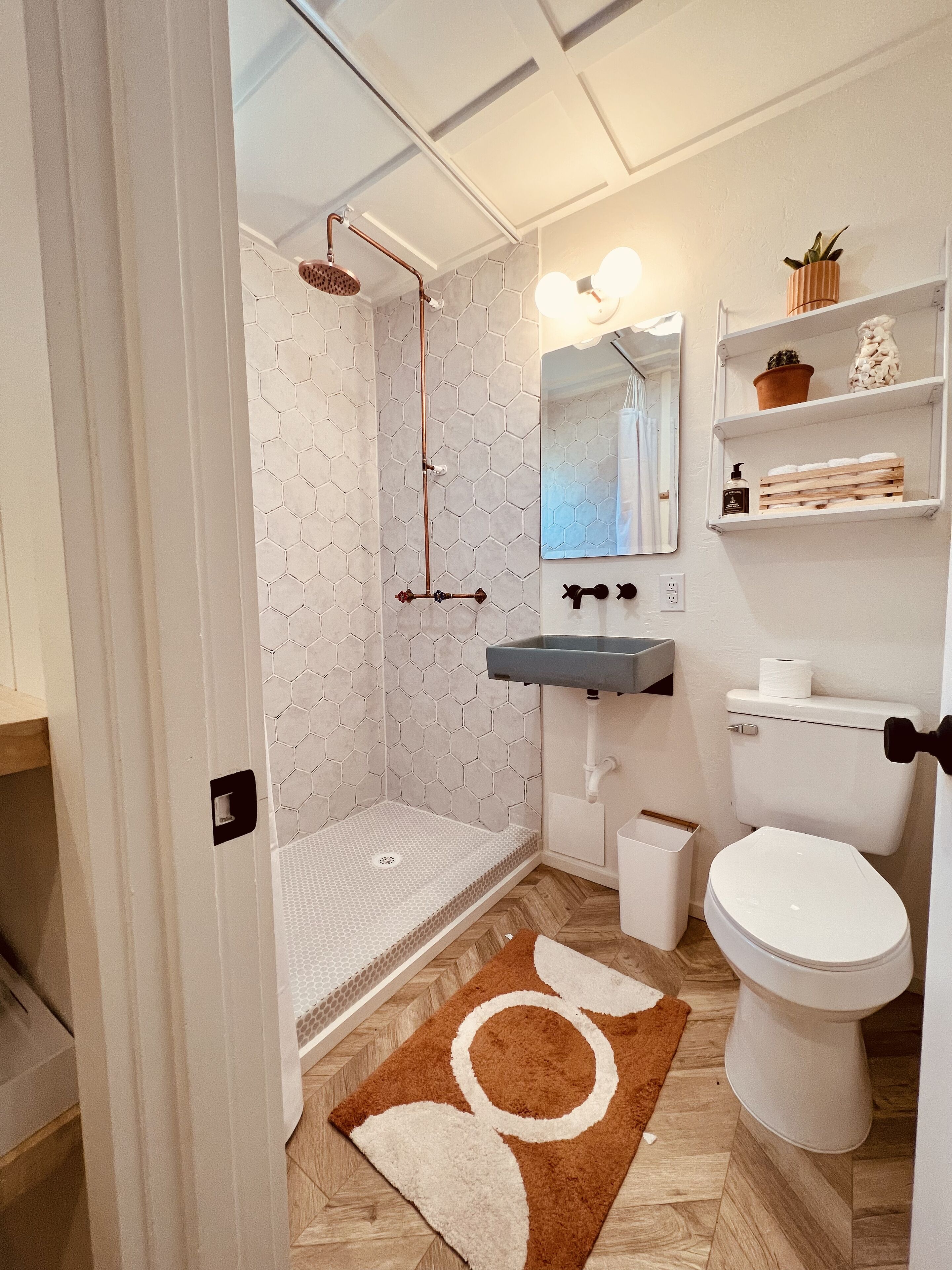 A bathroom with a shower, toilet, sink, and a mirror.