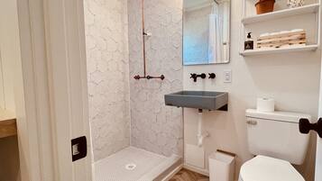A bathroom with a shower, toilet, sink, and a mirror.