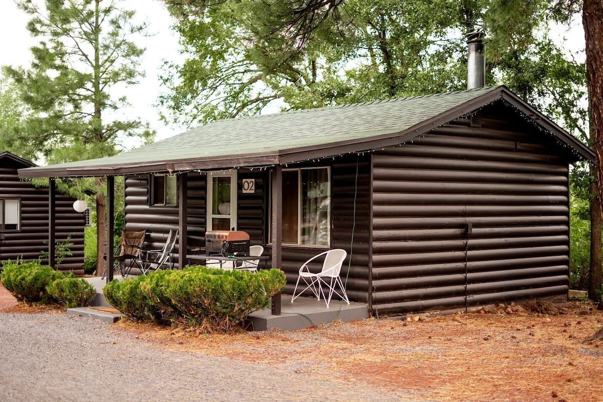 Eine Blockhütte mit Veranda, zwei Stühlen, einem Grill und einem Schild mit der Nummer 02.