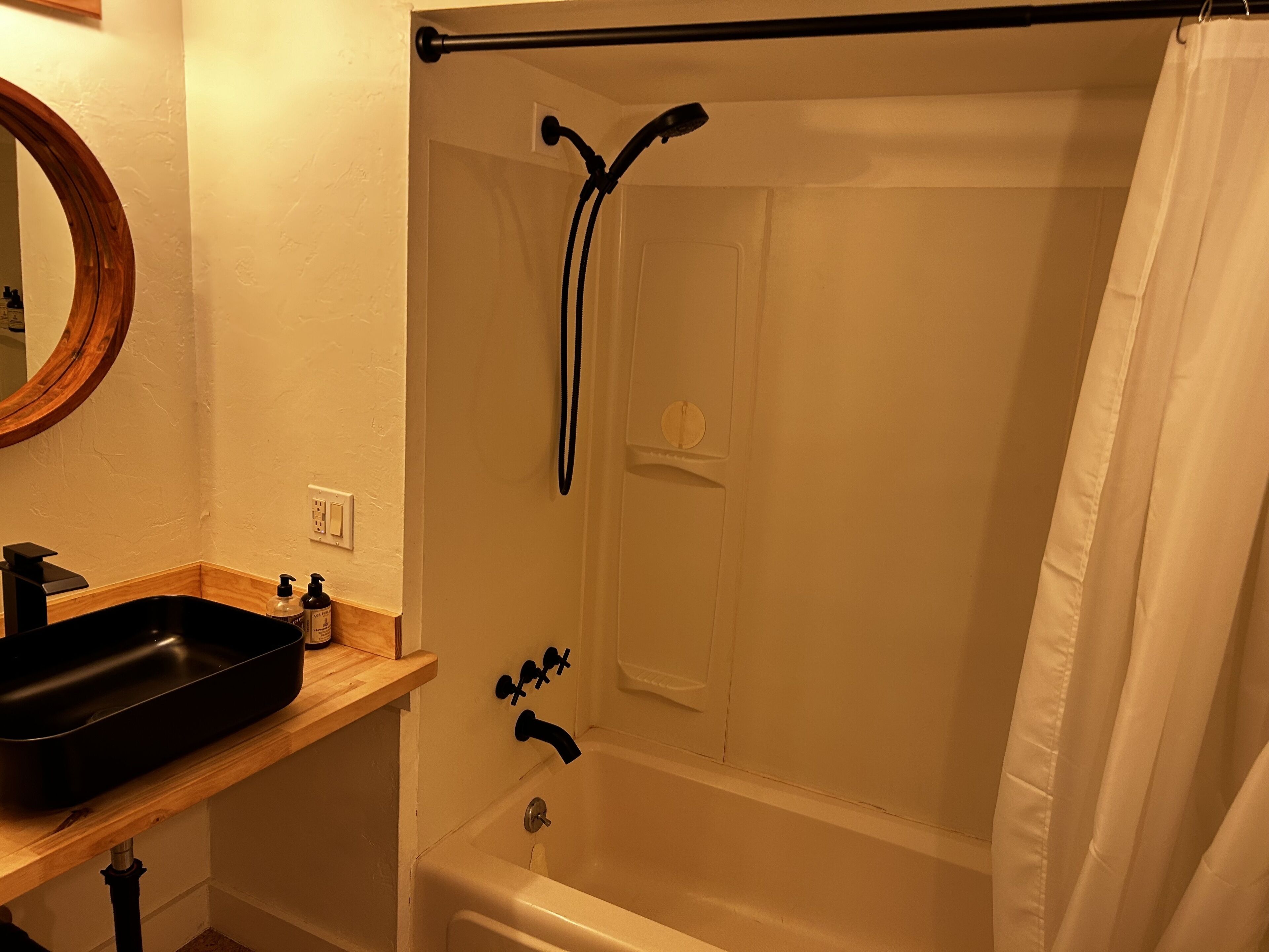 Un baño con bañera, ducha, lavabo con espejo y estante de madera.
