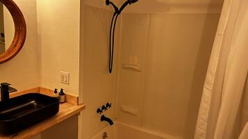 A bathroom with a bathtub, a shower, a sink with a mirror, and a wooden shelf.