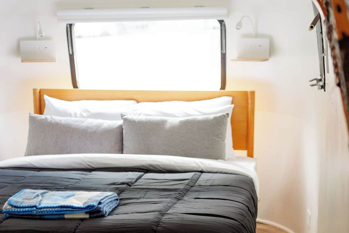 Ein Bett mit Holz Kopfteil, ein Fenster darüber und ein kleiner Tisch im Vordergrund.