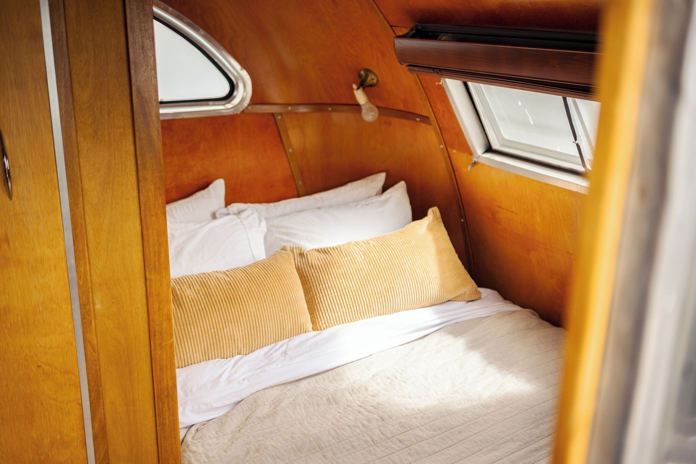 A compact, wooden interior with a bed featuring white and beige bedding.