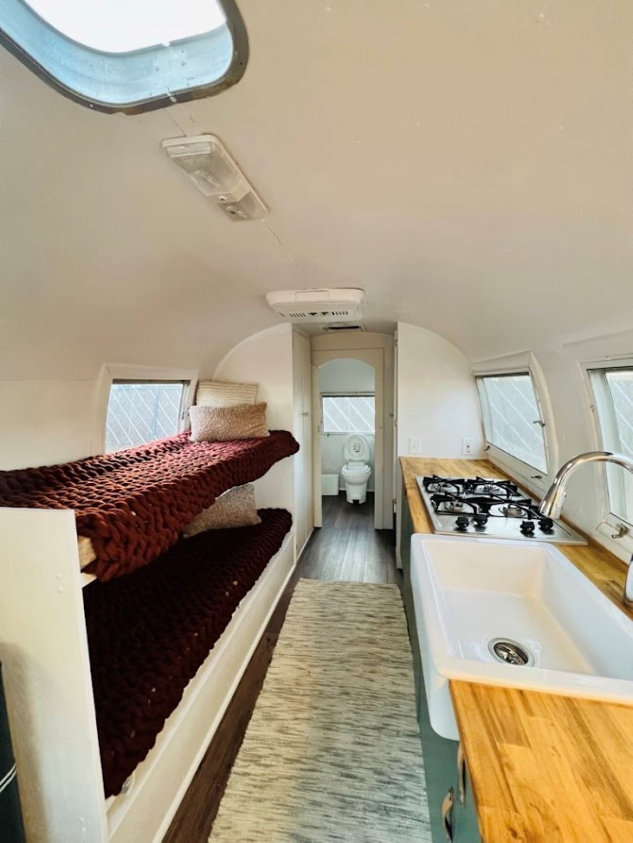 A compact RV interior with a kitchenette, a small bathroom, and a sleeping area with a bunk bed.