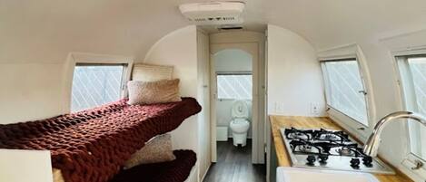A compact RV interior with a kitchenette, a small bathroom, and a sleeping area with a bunk bed.