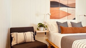 A bedroom with a bed, bedside table, lamp, and a chair. - Corduroy Boutique Lodge (Pinetop)