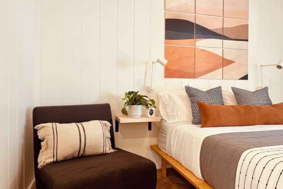 Ein Schlafzimmer mit einem Bett, einem Nachttisch, einer Lampe und einem Sessel.