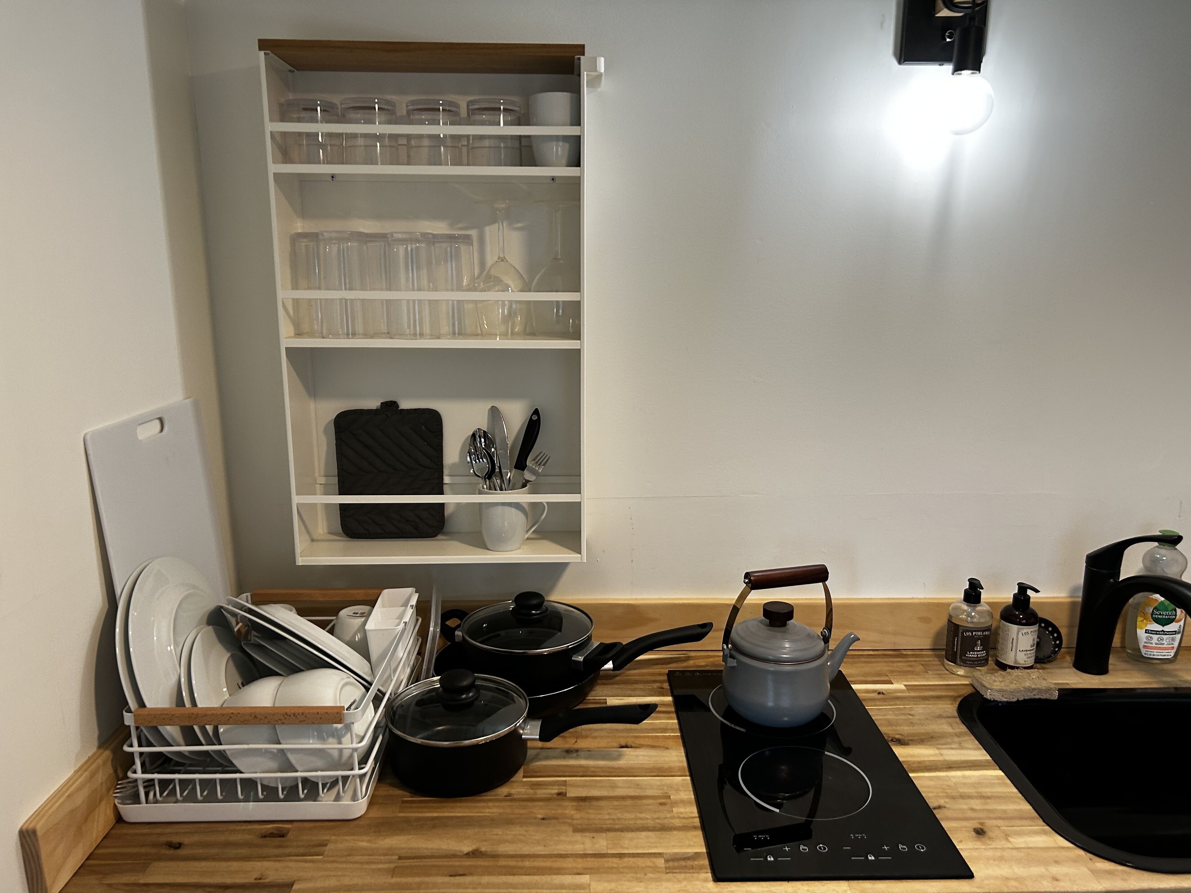 A kitchen with a wooden countertop, a black induction cooktop, a kettle, and a dish rack with dishes.