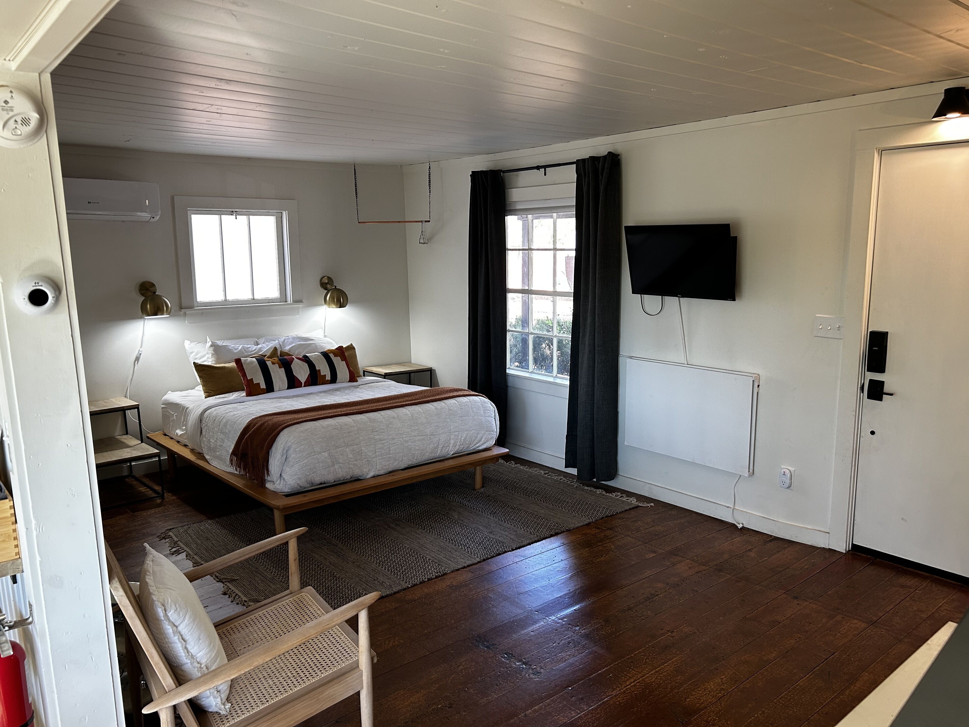 Une chambre à coucher comprenant un lit, des tables de chevet, un téléviseur fixé au mur et une fenêtre avec des rideaux.