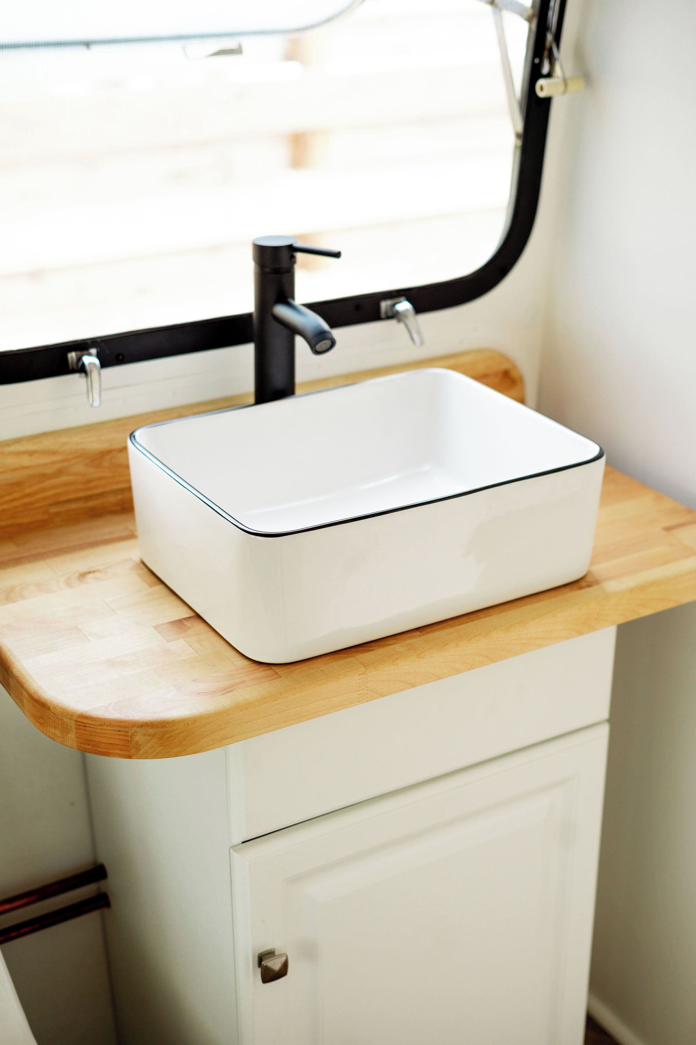 A white rectangular sink with a black rim on a wooden countertop, a black faucet, and a white cabinet below.