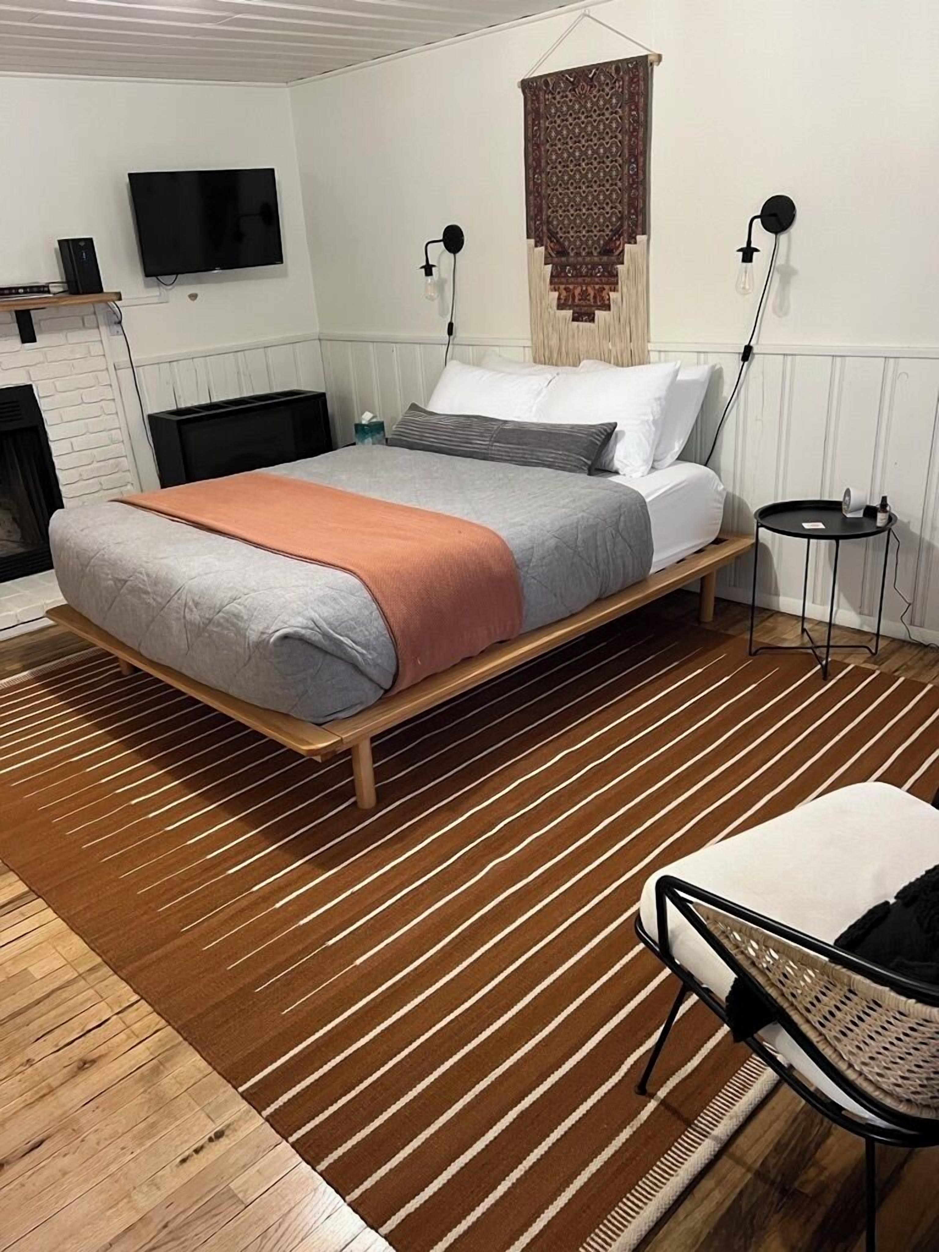A modern bedroom with a bed, a TV, a wall-mounted lamp, and a small side table.