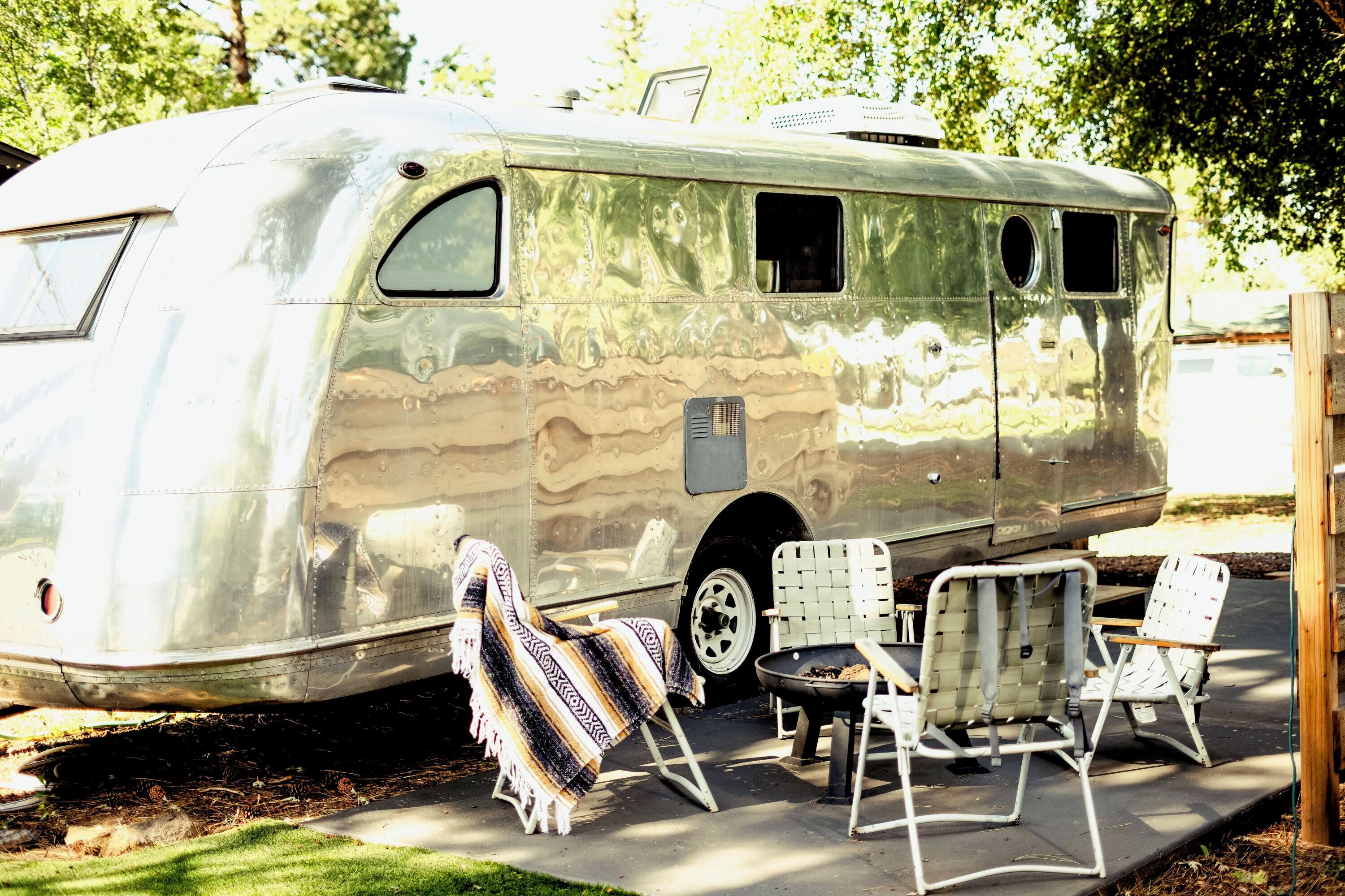Una furgoneta camper antigua estacionada en una zona sombreada con un espacio de estar cubierto y una pequeña mesa.