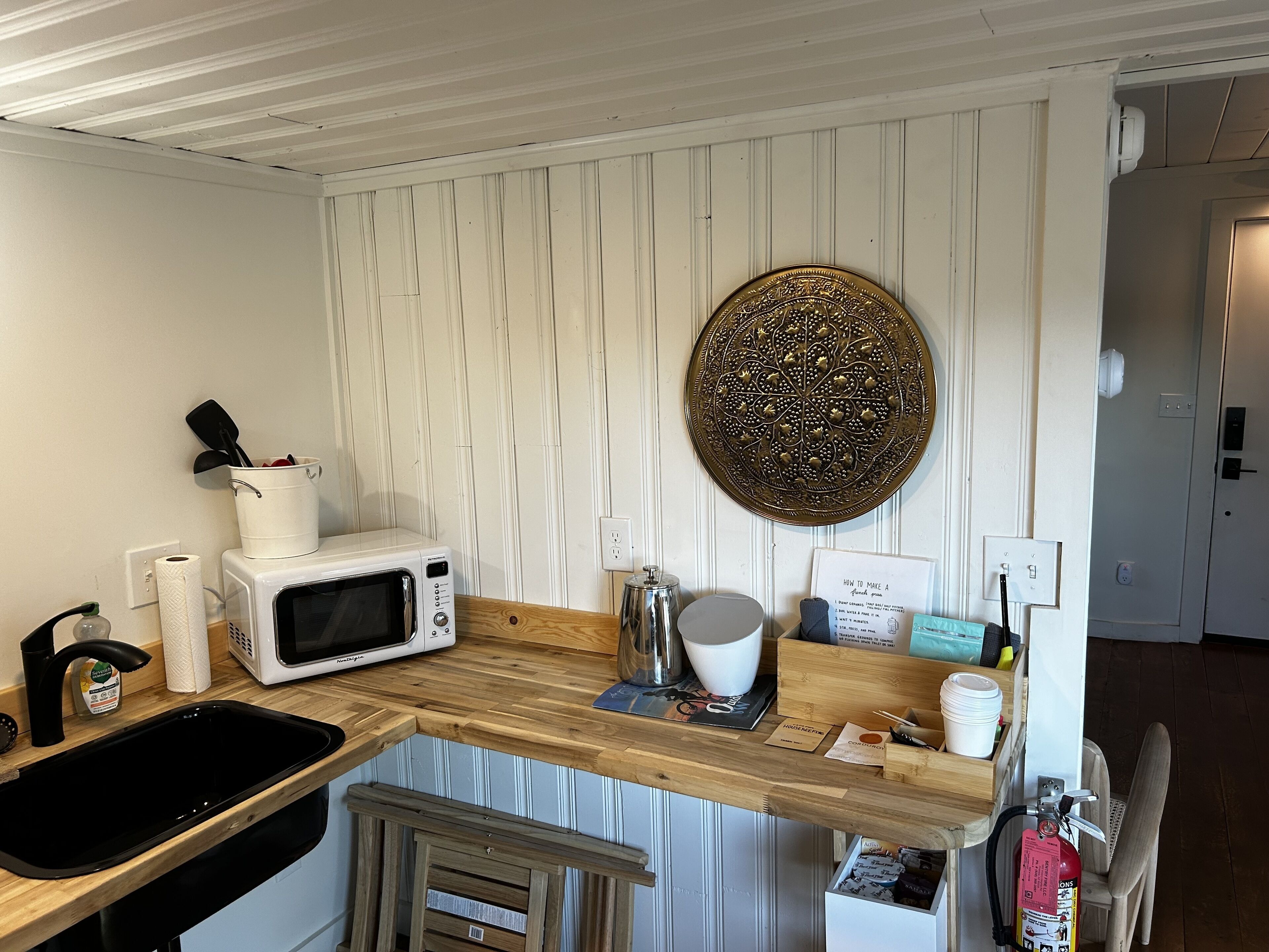 A kitchen with a wooden countertop, a white microwave, a coffee maker, and a fire extinguisher.