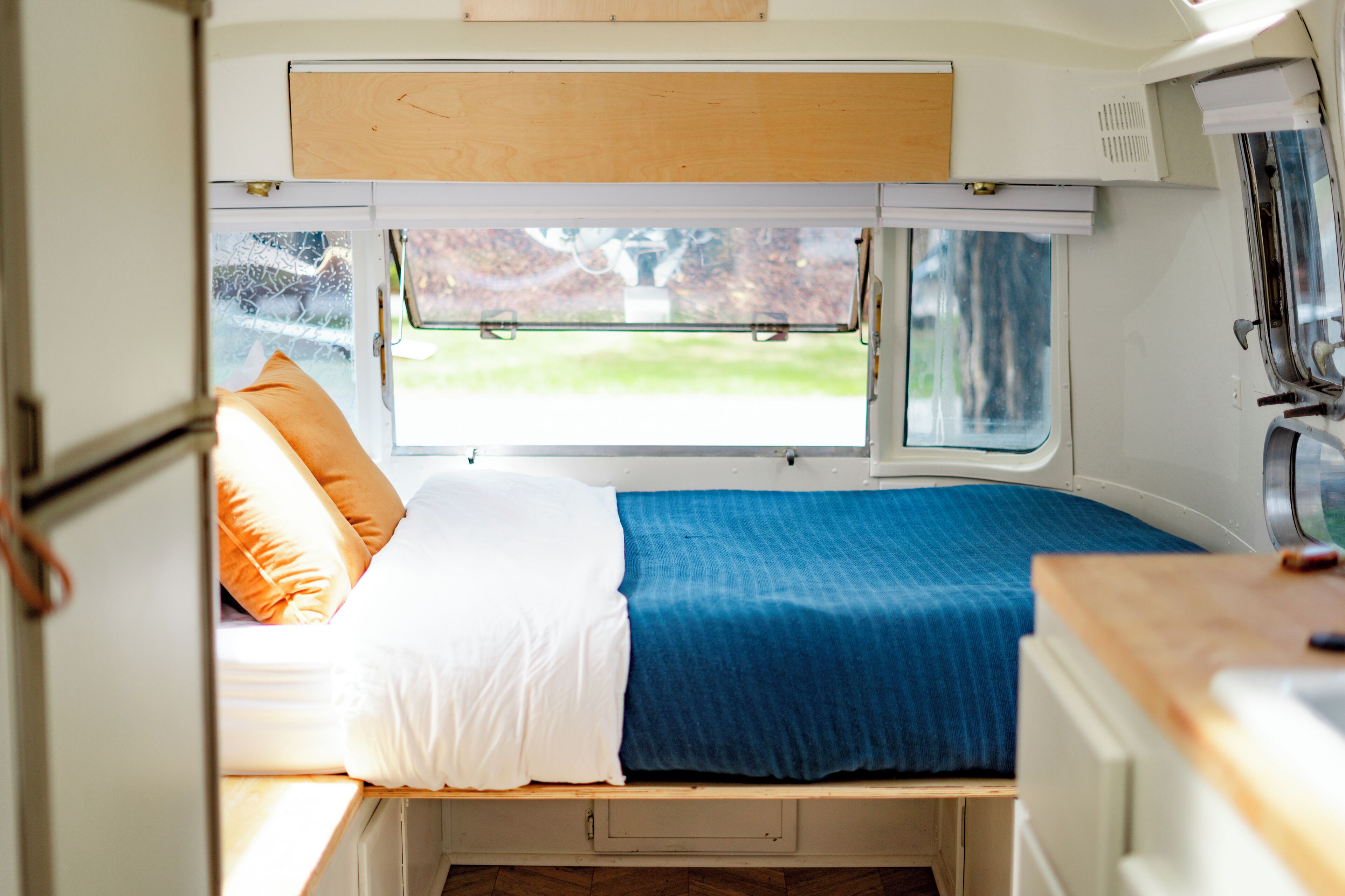 A compact RV interior with a bed, a window, and a kitchenette area.