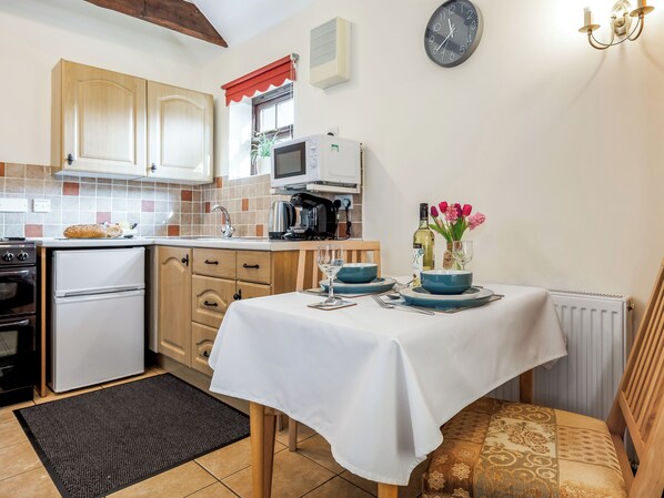 A compact kitchen with wooden cabinets, a microwave, a coffee maker, and a dining table set for two.