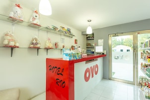 A hotel reception area with a red counter, shelves with various items, and a view of the outside through a glass door.